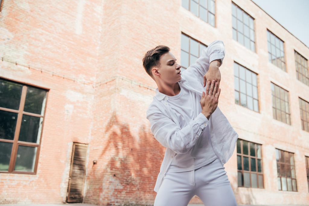 pohledný mladý muž v bílých šatech tančí na ulici - Fotografie, Obrázek