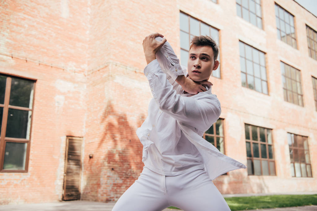 молодий чоловік у білому одязі танцює на міській вулиці
    - Фото, зображення