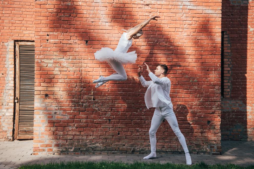side view of beautiful young couple of dancers performing ballet dance on city street - Photo, Image