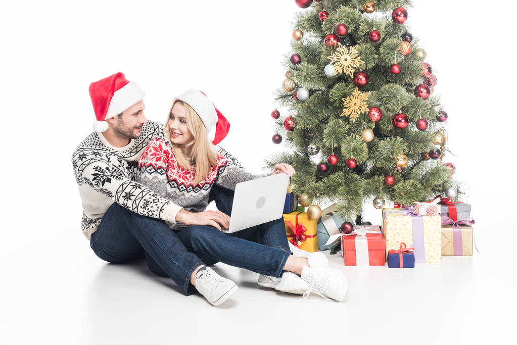 iki Noel Baba şapkaları ile Noel ağacı üzerinde beyaz izole yakınındaki laptop içinde gülümseyen - Fotoğraf, Görsel