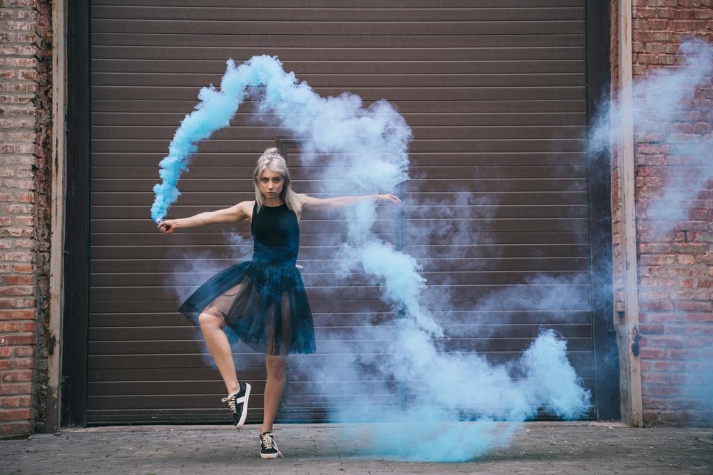 girl dancing in blue smoke and looking at camera on urban city street - Photo, Image