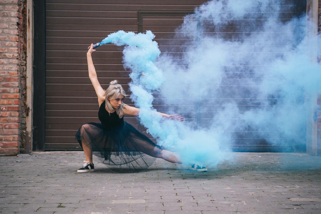 молодая танцовщица танцует в голубом дыму на улице
  - Фото, изображение