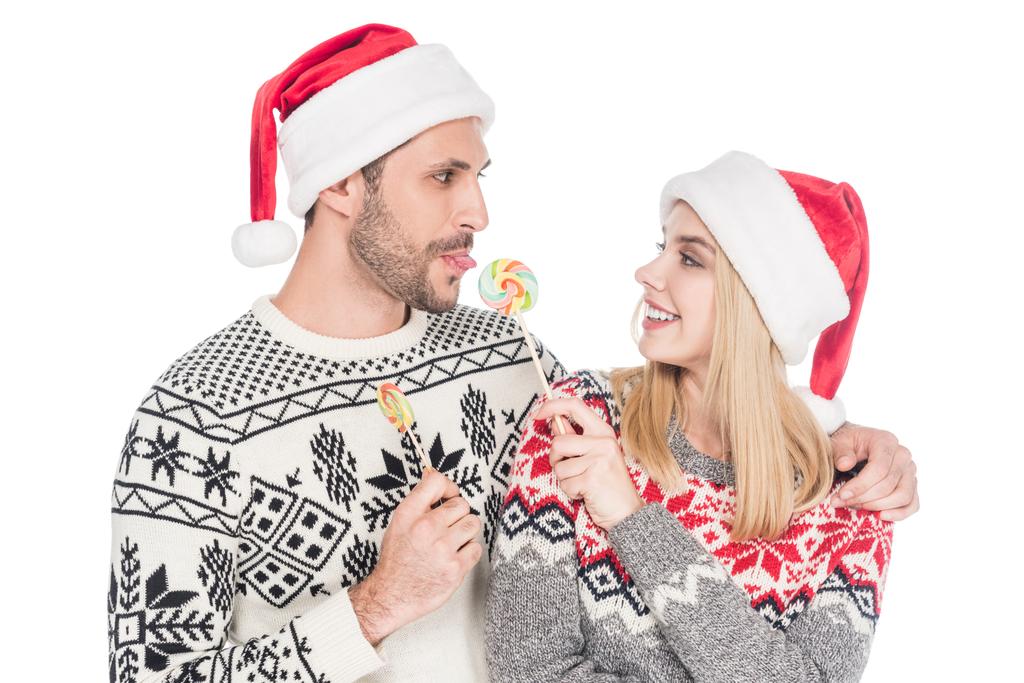 ritratto di giovane coppia caucasica in cappelli di Babbo Natale con lecca-lecca isolati su bianco
 - Foto, immagini