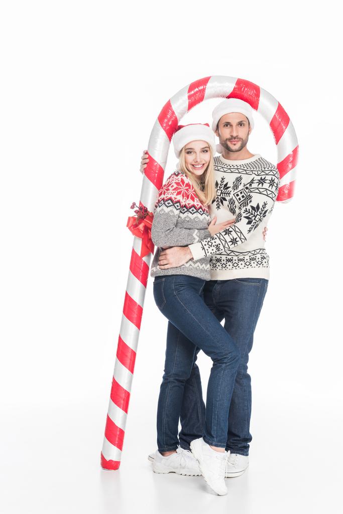joven pareja en santa claus sombreros y suéteres con juguete caramelo aislado en blanco
 - Foto, Imagen
