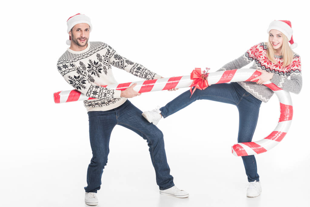 молодая пара в шляпах и свитерах Санта-Клауса останавливает игрушечные конфеты, изолированные на белом
 - Фото, изображение
