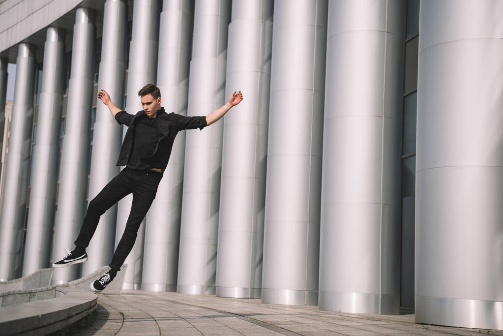 knappe jongeman in zwarte kleding springen in dans op straat  - Foto, afbeelding