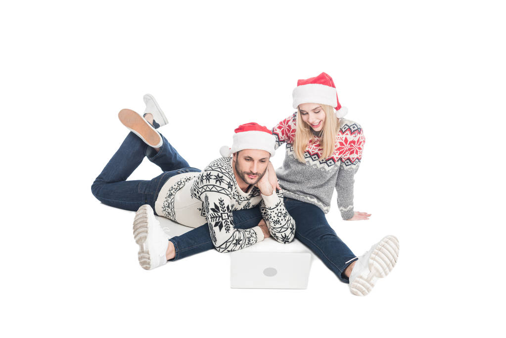 pareja joven en suéteres y sombreros de santa claus con portátil aislado en blanco
 - Foto, Imagen