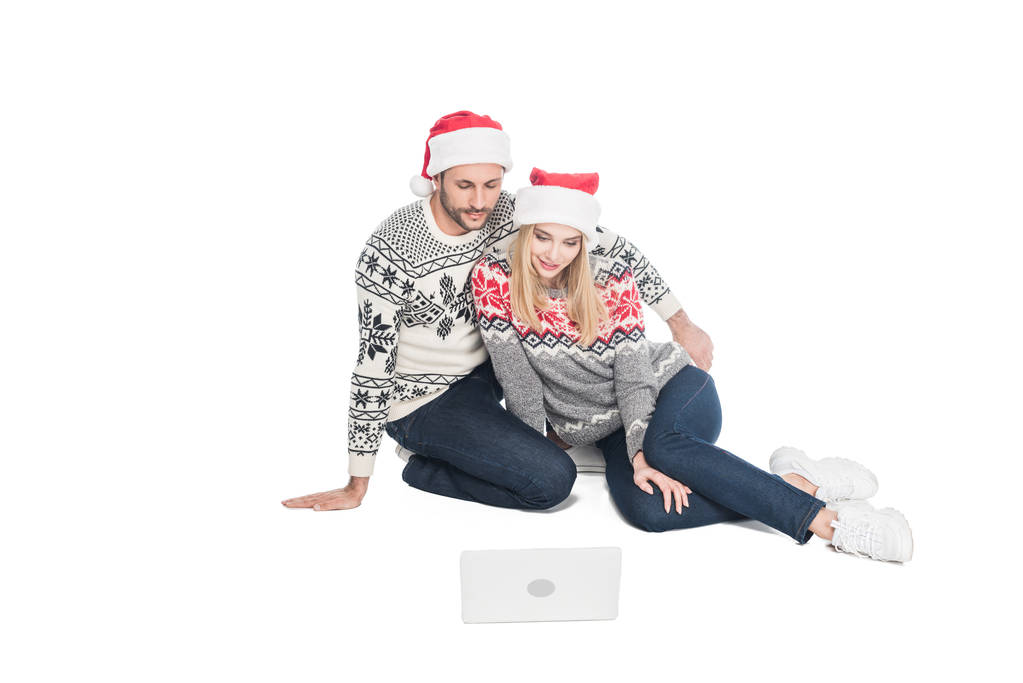 young couple in sweaters and santa claus hats with laptop isolated on white - Photo, Image