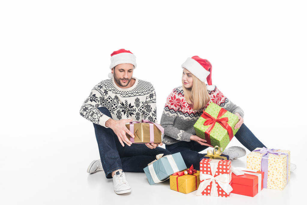 para w swetry i czapki Mikołaja z prezentami zawinięty, siedząc na podłodze, na białym tle - Zdjęcie, obraz