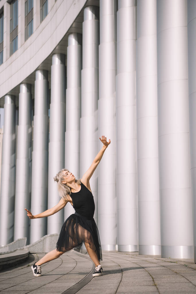 привлекательная девушка в черной юбке танцует возле колонн на улице
 - Фото, изображение