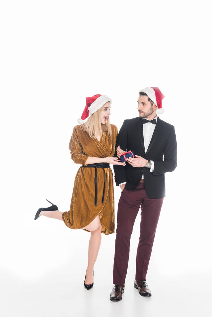 κομψό νεαρό ζευγάρι στο Βασίλη καπέλα με τυλιγμένο χριστουγεννιάτικο δώρο που απομονώνονται σε λευκό - Φωτογραφία, εικόνα