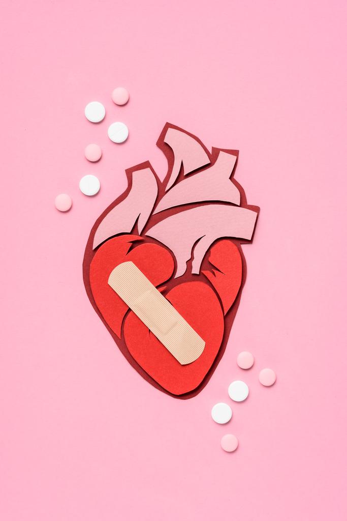 Ansicht des anatomischen menschlichen Herzens mit Pflaster und Pillen auf rosa  - Foto, Bild