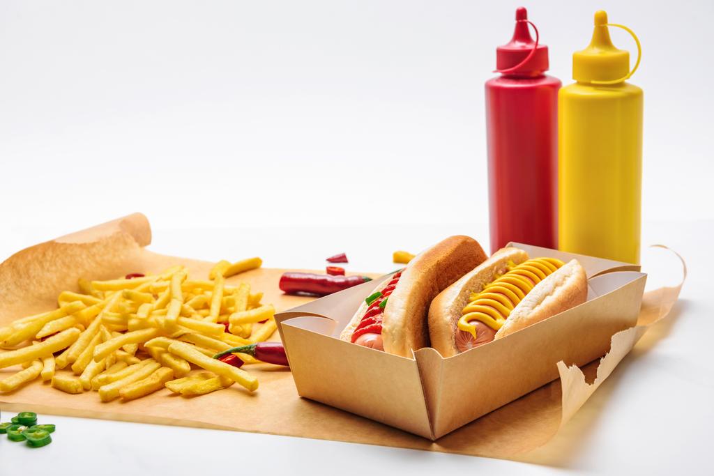 Nahaufnahme von leckeren Hot Dogs mit Pommes auf Papier und auf Weiß - Foto, Bild