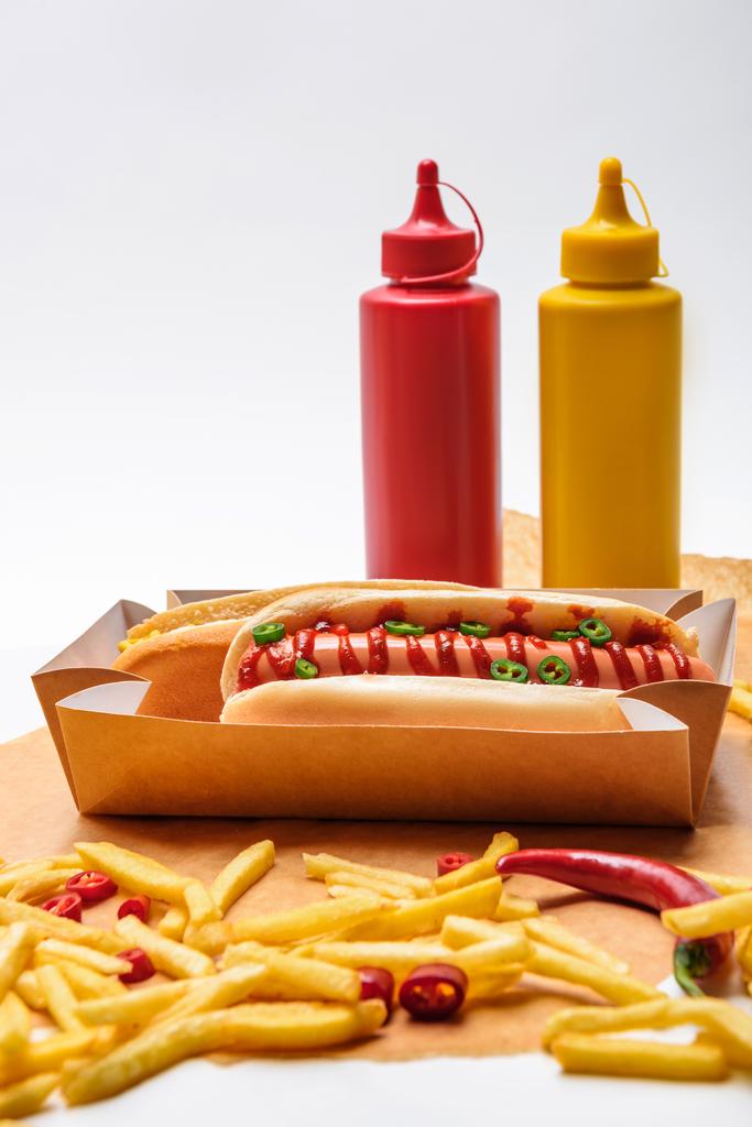 primer plano de deliciosos hot dogs con papas fritas, mostaza y ketchup sobre papel sobre superficie blanca
 - Foto, Imagen