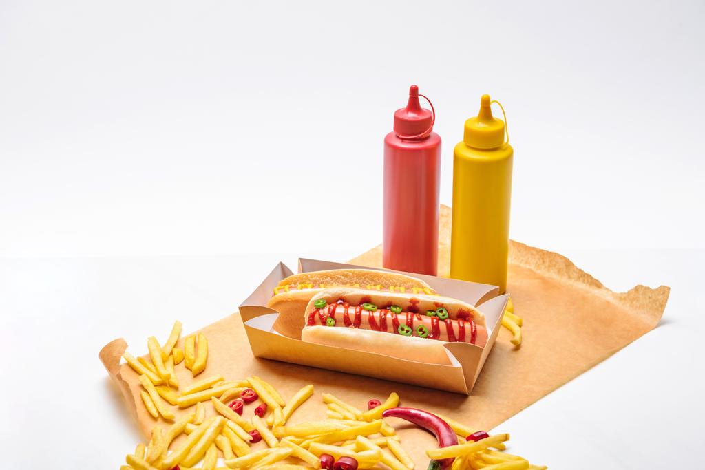 close-up de cachorros-quentes com batatas fritas, mostarda e ketchup em papel na superfície branca
 - Foto, Imagem