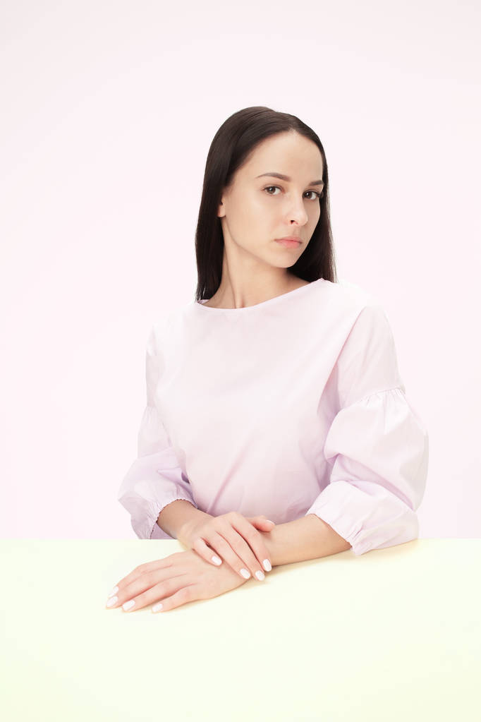 Femme d'affaires sérieuse assise à une table sur un fond rose
 - Photo, image