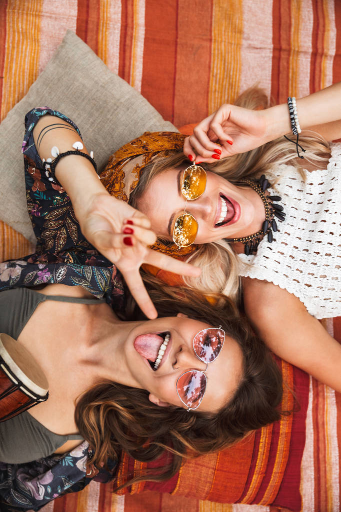 Foto von oben auf zwei junge Hippie-Mädchen lächelnd und auf Decke im Freien Kopf an Kopf liegend - Foto, Bild