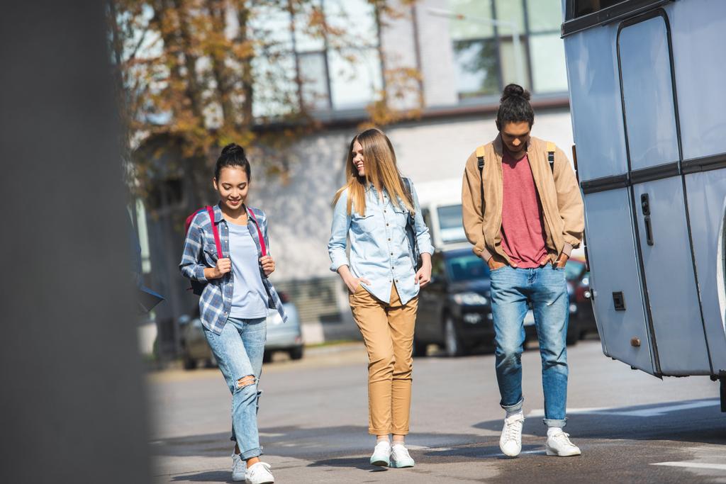 enfoque selectivo de jóvenes amigos multiétnicos con mochilas caminando cerca de autobús en la calle de la ciudad
  - Foto, Imagen
