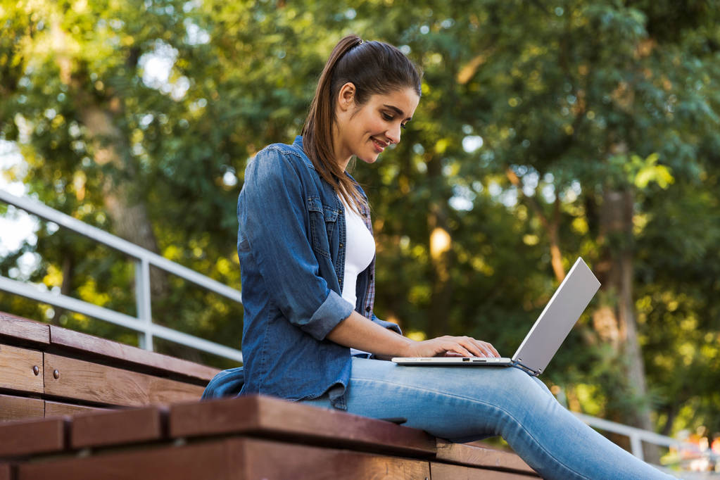 Immagine di sorprendente giovane bella donna seduta all'aperto utilizzando il computer portatile
. - Foto, immagini