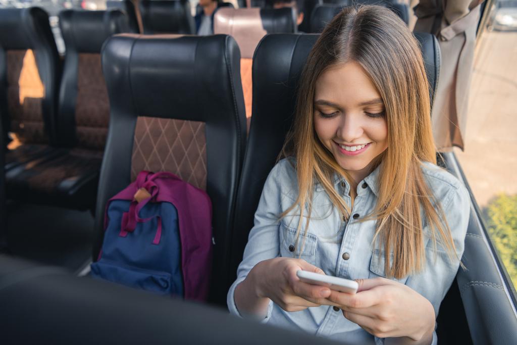 feliz jovem mulher usando smartphone enquanto sentado em ônibus de viagem
  - Foto, Imagem
