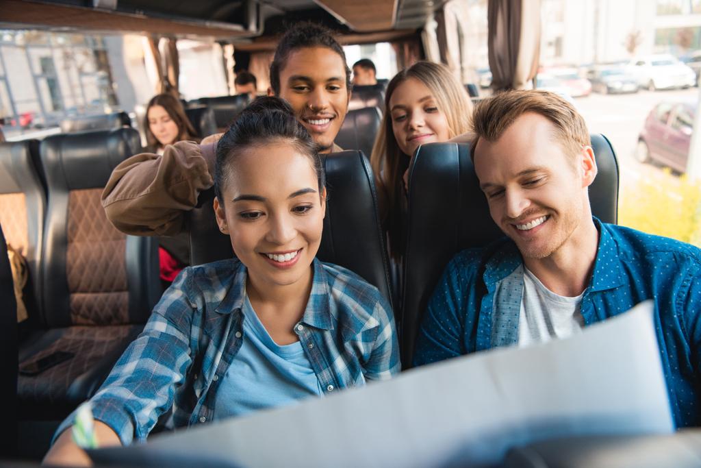 fröhliche multiethnische Touristen, die während einer Busfahrt auf die Landkarte schauen - Foto, Bild