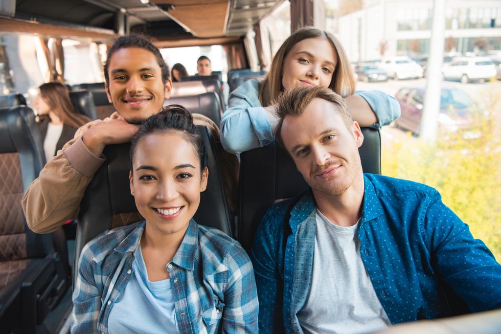 Porträt glücklicher multikultureller Freunde, die während einer Busfahrt in die Kamera blicken  - Foto, Bild
