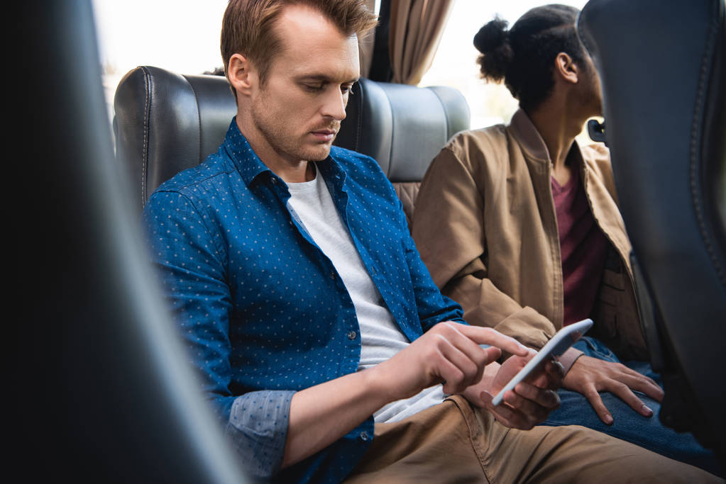 dospělý muž pomocí smartphone, zatímco jeho přítel sedí poblíž v cestování autobusem  - Fotografie, Obrázek