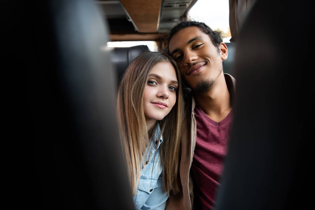 selective focus of young interracial couple looking at camera during trip on travel bus - Photo, Image
