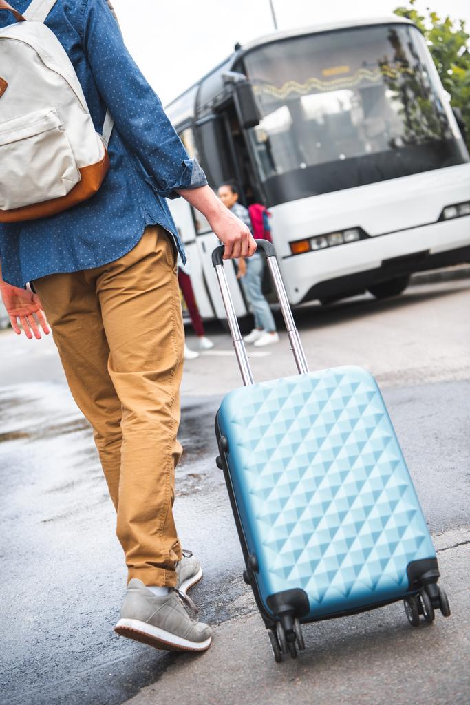image recadrée de l'homme avec sac à dos portant sac à roulettes près de bus de voyage à la rue
 - Photo, image