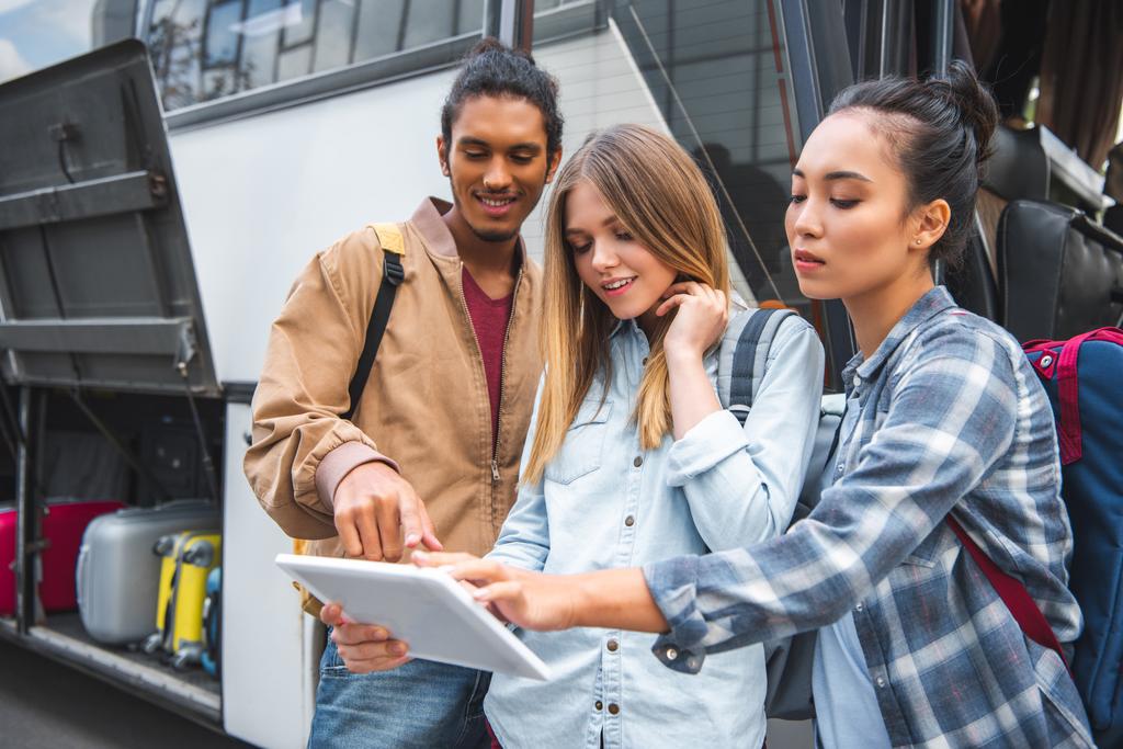 joven de raza mixta apuntando a la tableta digital a las amigas cerca de autobús de viaje en la calle de la ciudad
  - Foto, imagen