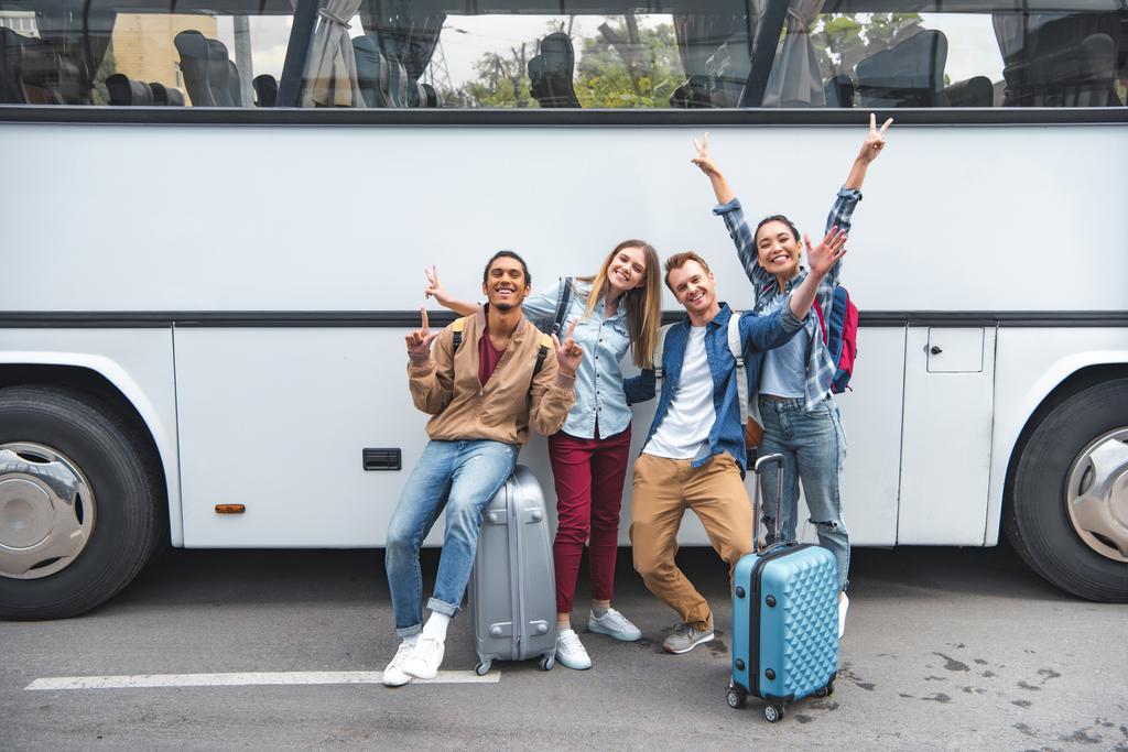 turisti multietnici allegri con borse da viaggio che fanno segni di pace vicino all'autobus in strada
 - Foto, immagini