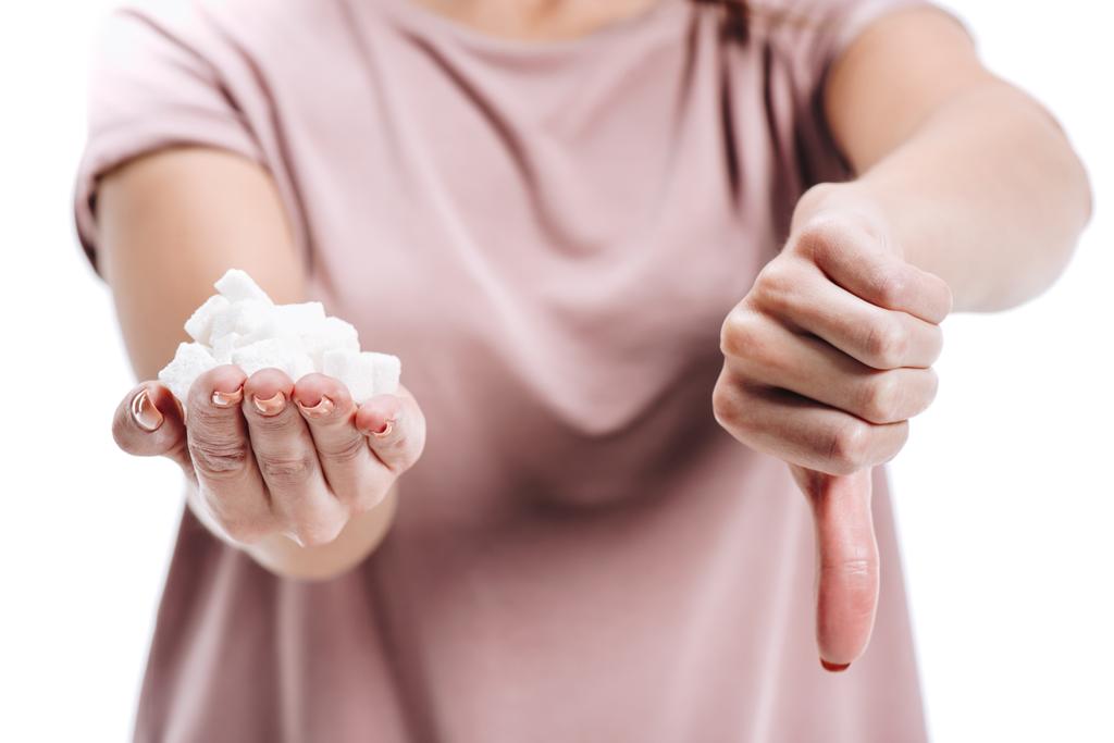 corte close up de mulher segurando açúcar branco não saudável e mostrando polegar para baixo isolado no branco
 - Foto, Imagem