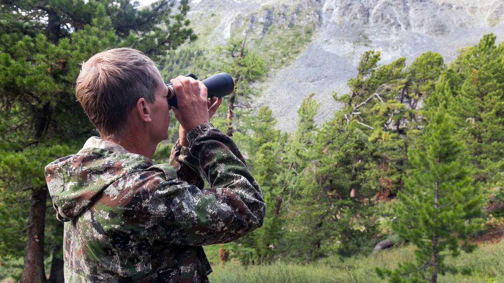 Un hombre mira en un telescopio a la cima de la montaña. El turista mira a través de los prismáticos a las montañas
. - Foto, Imagen