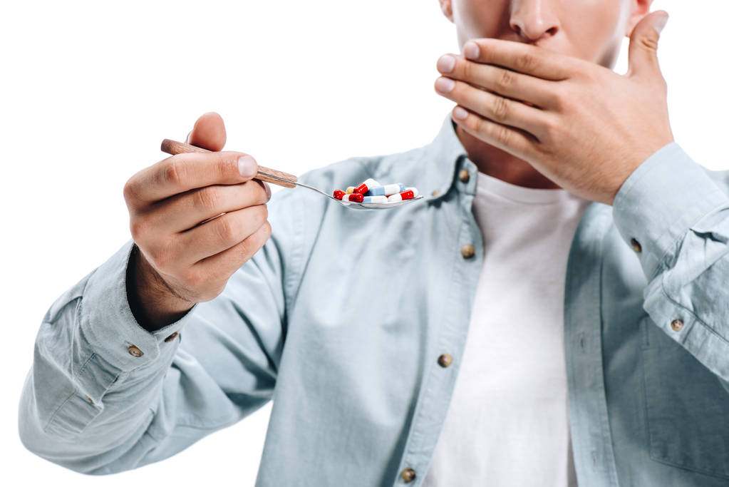bijgesneden afbeelding van man die betrekking hebben op mond en lepel van pillen geïsoleerd op wit te houden - Foto, afbeelding