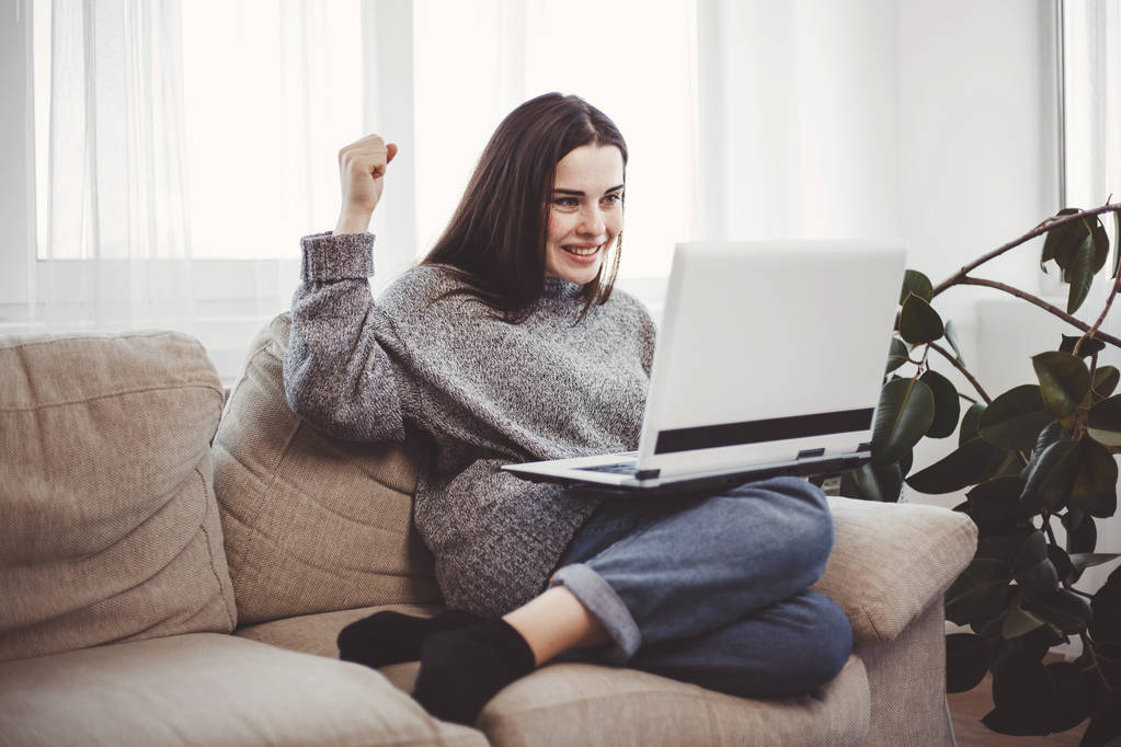 Mujer excitada joven usando el ordenador portátil en la sala de estar
 - Foto, Imagen