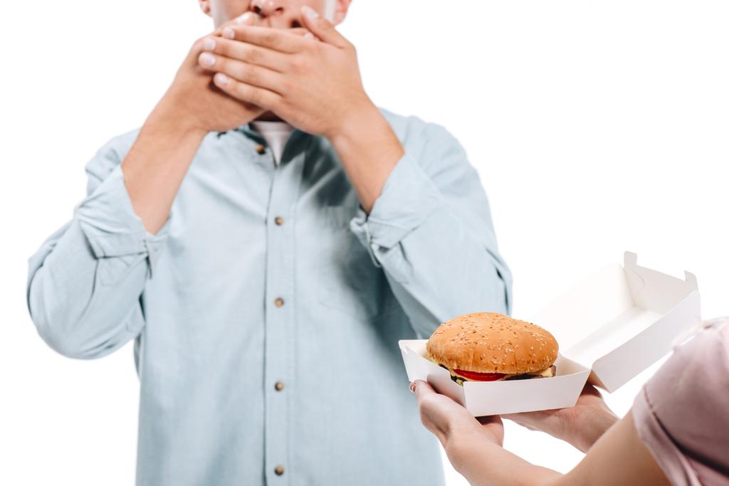 imagen recortada de hombre cubriendo la boca, mujer proponiendo hamburguesa aislada en blanco
 - Foto, imagen