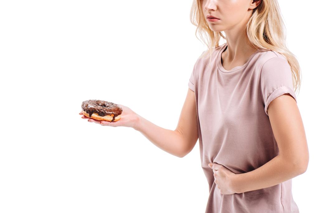 mide ağrısı gösterilen ve çikolatalı çörek üzerinde beyaz izole tutan kadının kırpılmış görüntü - Fotoğraf, Görsel
