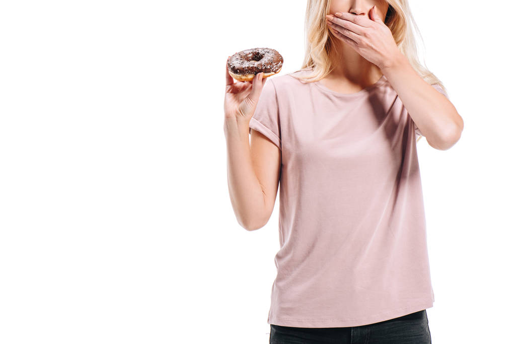 abgeschnittenes Bild einer Frau, die Schokoladenkekse in der Hand hält und den Mund isoliert auf weißem Papier bedeckt - Foto, Bild