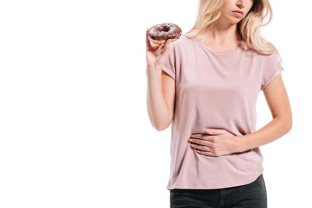 cropped image of woman showing stomach pain and holding doughnut isolated on white - Photo, Image