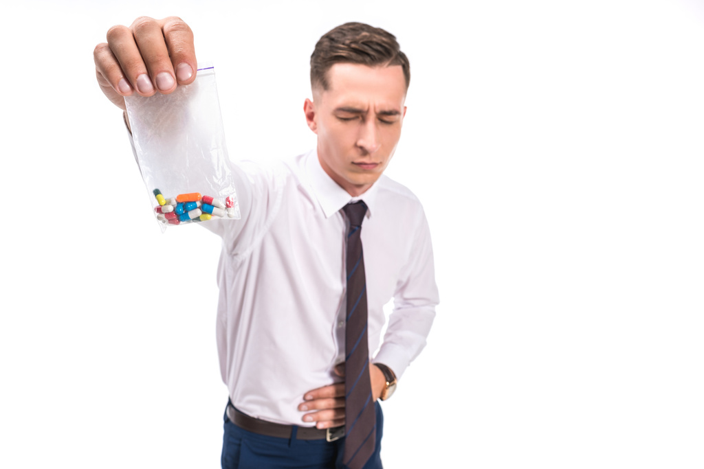 вибірковий фокус бізнесмена, що показує біль у шлунку і тримає кольорові таблетки від наркотиків ізольовані на білому
 - Фото, зображення