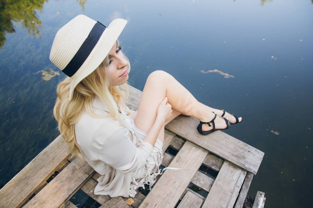 Hermosa joven rubia en un sombrero descansando en el lago de otoño en el puente. Tonificación
. - Foto, imagen