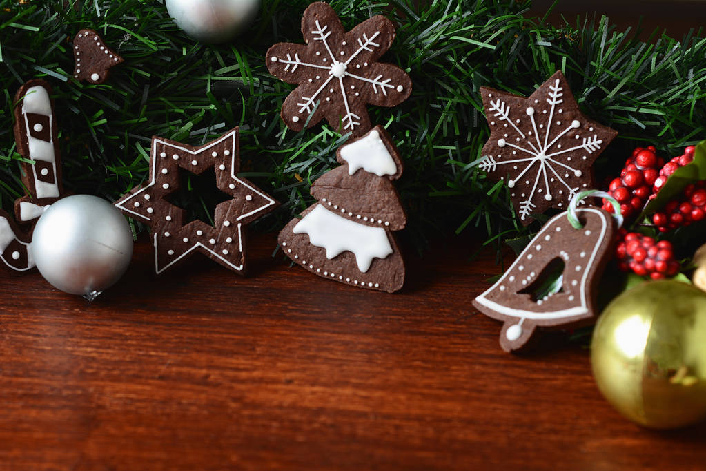 Κλείνω πάνω θέα των Χριστουγέννων cookies που κρέμεται κάτω από την εορταστική κλαδιά έλατου ξύλινο τραπέζι. Χριστουγεννιάτικες διακοπές έννοια. - Φωτογραφία, εικόνα