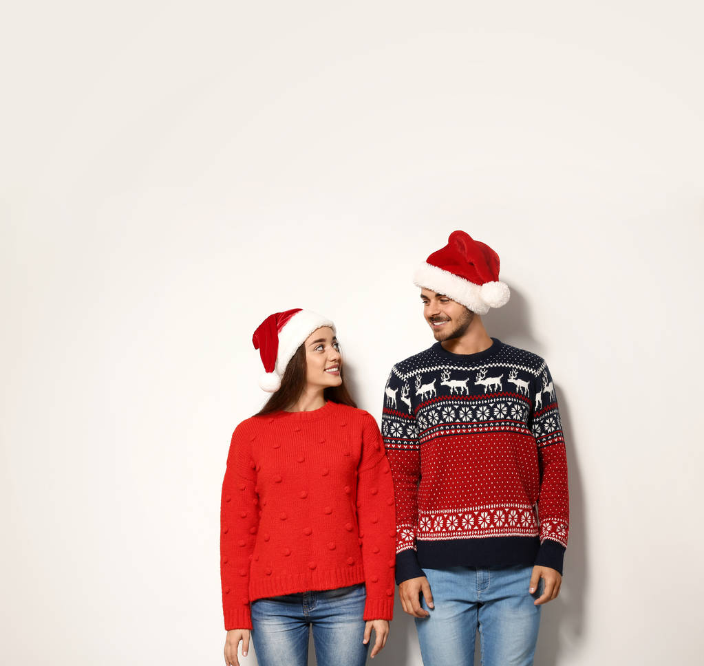 Молода пара в теплих светрах і різдвяних капелюхах на білому тлі
 - Фото, зображення