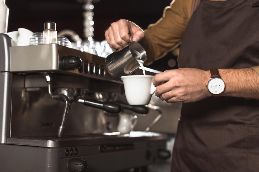 abgeschnittene Aufnahme eines Barista, der Milch in Kaffee gießt, während er sie im Café zubereitet - Foto, Bild