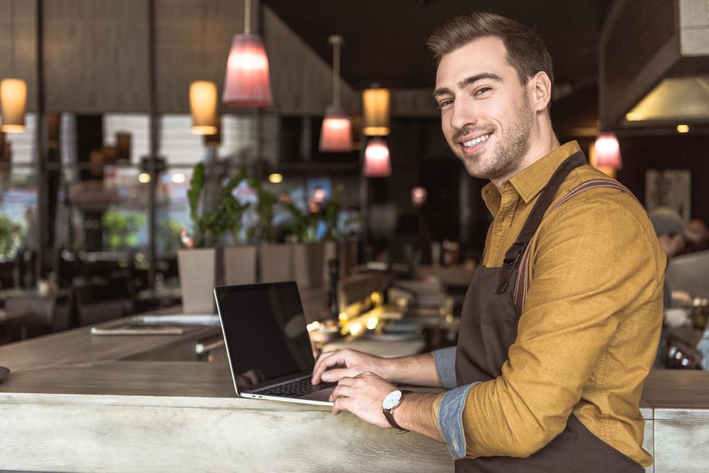 komea nuori tarjoilija käyttää kannettavaa tietokonetta baaritiski kahvilassa
 - Valokuva, kuva