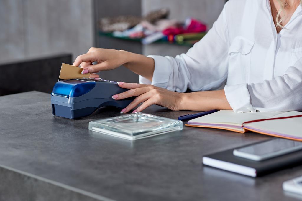 tiro recortado de joven vendedora con tarjeta de crédito y el uso de terminal de pago en la tienda
 - Foto, Imagen