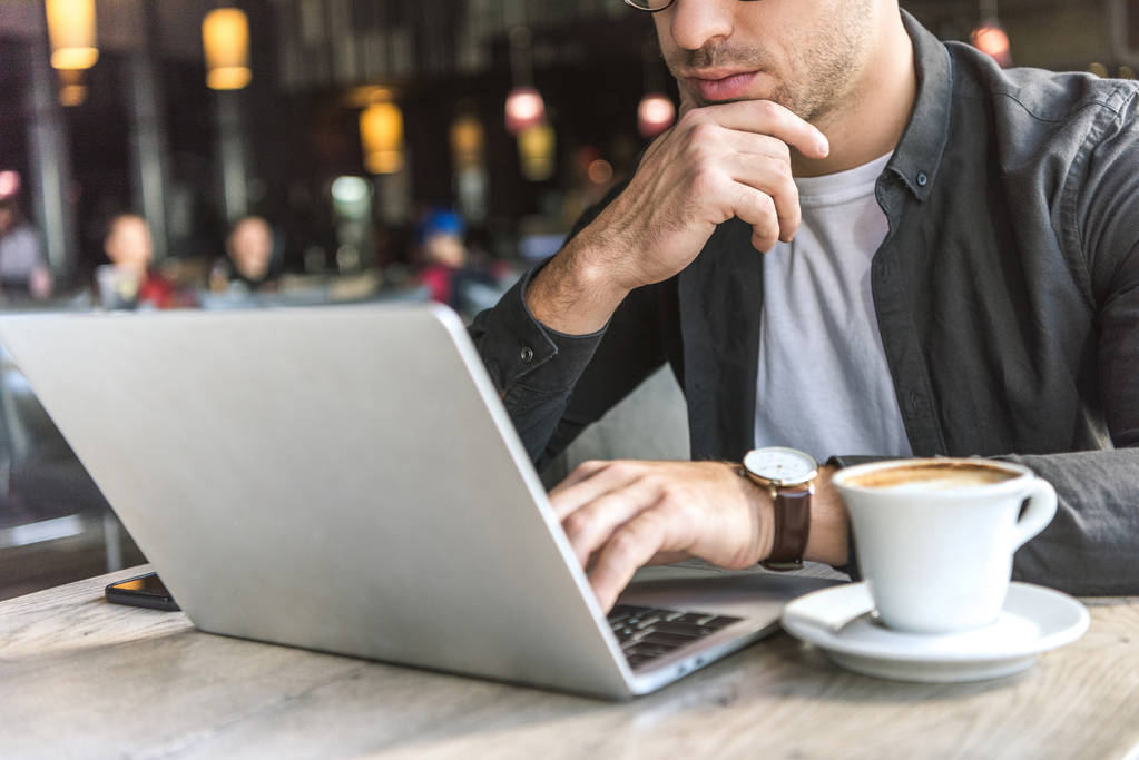 tiro recortado de jovem freelancer trabalhando com laptop no café com xícara de café na mesa
 - Foto, Imagem