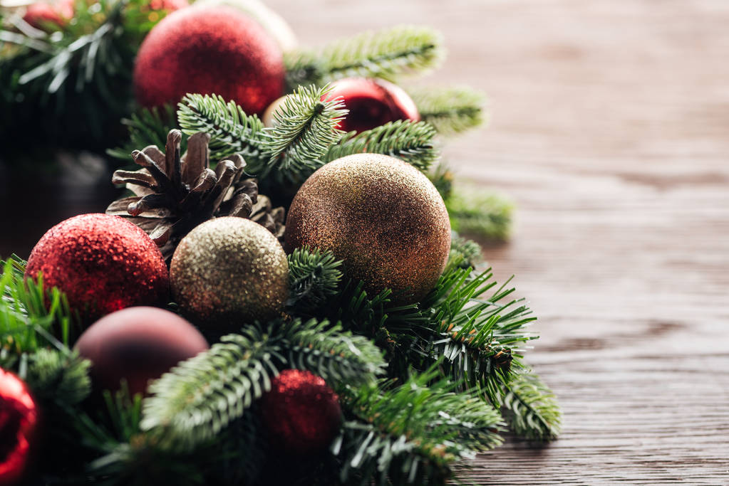 закрытый вид на сосновый венок с красными и золотыми рождественскими шарами на деревянном фоне
 - Фото, изображение