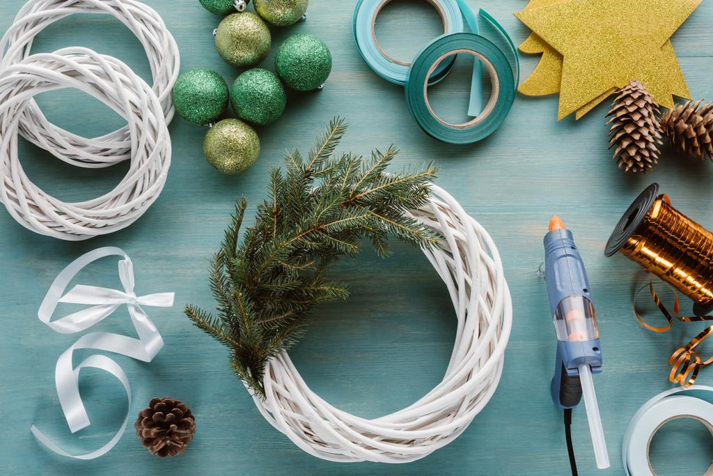 плоский лежак з влаштованою клейовою пістолетом, різдвяними іграшками та прикрасами для різдвяного вінка ручної роботи на синій дерев'яній стільниці
 - Фото, зображення