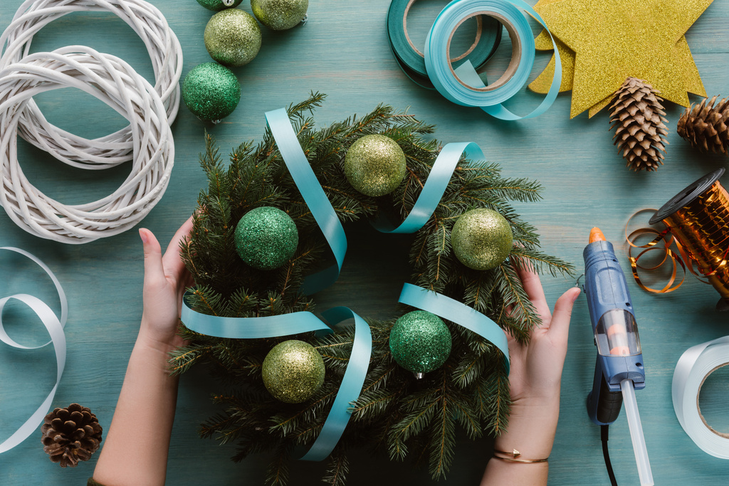 обрізаний знімок жінки з різдвяним вінком ручної роботи, прикрашений стрічкою та іграшками на синій дерев'яній поверхні
 - Фото, зображення